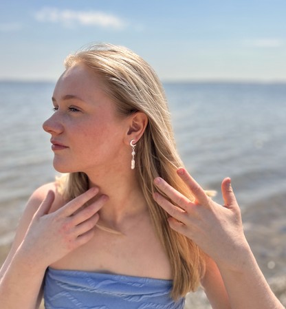 Billede af en kvinde iført sølvøreringe med måne, sol og perlevedhæng fra VILMA, fotograferet ved havet i dagslys